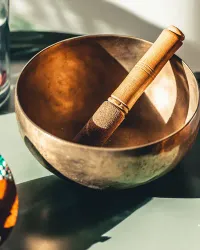 A copper singing bowl with a wooden mallet in warm sunlight