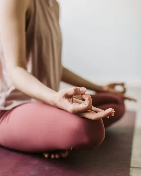 A person seated cross-legged in a mudra, wearing a rose-coloured top and leggings by a softly lit window